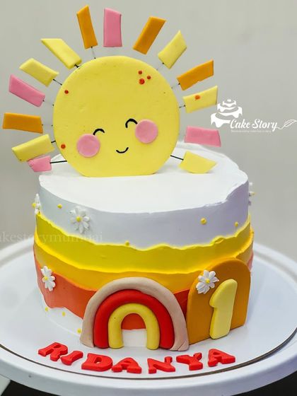 A sunshine-themed cake for a first birthday. This cake features a cute smiling sun, a small rainbow, and warm, sunny colors.