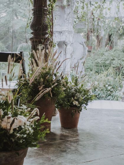 Potted grasses and white flowers line the aisle of our 'Love in Ruins' wedding. The decor is intentionally understated and natural, designed to complement the venue's rustic stone pillars and lush surroundings.