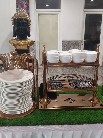 Organization is key in a buffet line. This station features neatly stacked plates, bowls, and cutlery in stylish copper-toned stands, ensuring easy access for guests.