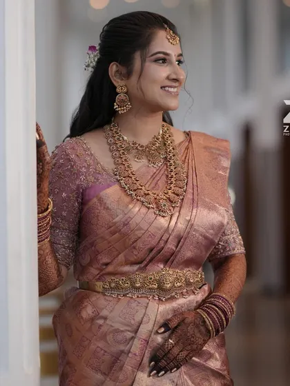 This bride looks lovely in a dusty rose Kanchivaram saree. Her blouse is fully embroidered with delicate beadwork, adding a subtle shimmer to her muhurtham look.