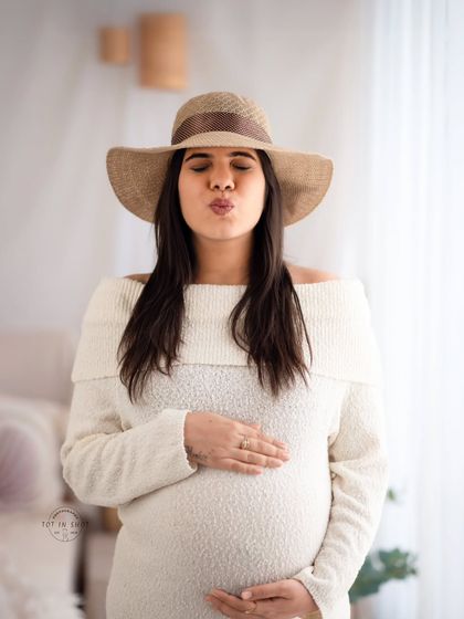A fun and playful solo portrait of a mom-to-be in a cozy sweater dress and a stylish hat.
