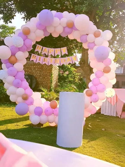 A beautiful balloon ring setup for an outdoor garden party. The pastel purple, pink, and white balloons look great in the natural light, creating a perfect backdrop for photos.