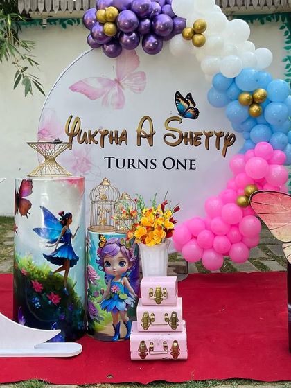 A magical butterfly and fairy theme for a first birthday. This outdoor setup includes a personalized circular backdrop, a pastel balloon garland, and themed props like a crescent moon and fairy cutouts.