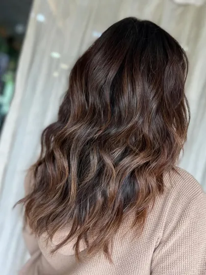 The back view of this glossy brown mane. The soft, undone waves give it a modern and relaxed feel, while the colour remains rich and luxurious.