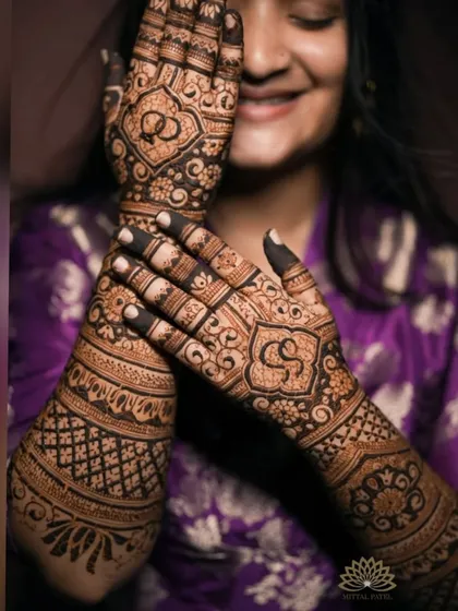 A happy client showing off her engagement mehndi, which includes personalized initials and interlocking rings.