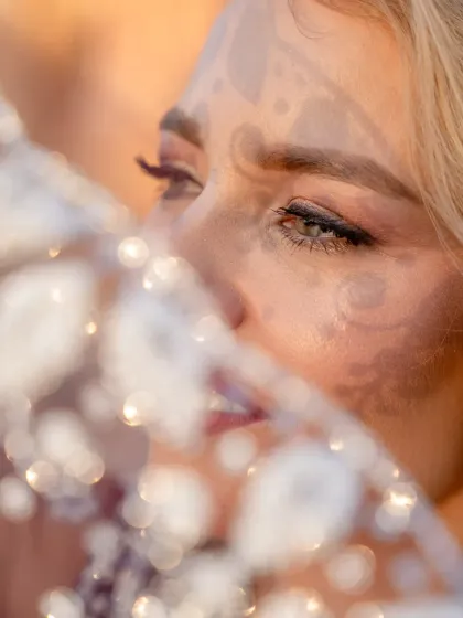An artistic close-up shot through the sheer, sparkling fabric of the dupatta. This creative composition focuses on the model's eyes, adding a layer of mystery and beauty.