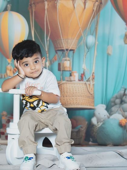 A cute toddler strikes a thoughtful pose on a toy tricycle against a hot air balloon backdrop.