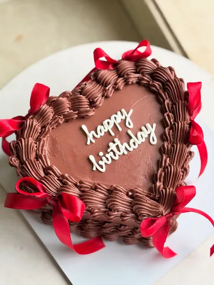 An aerial view of the chocolate heart birthday cake, emphasizing the contrast between the dark chocolate frosting and the bright red ribbons.