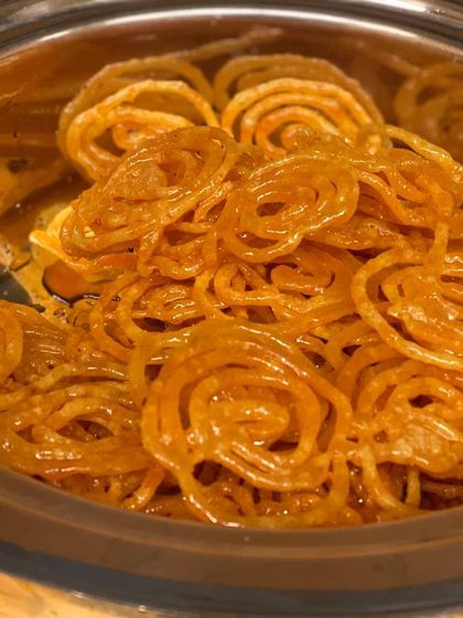 A close-up of our perfectly golden jalebis, soaked in sweet syrup. This classic Indian dessert is a must-have for celebrations, and we make sure each one is crispy and delicious.