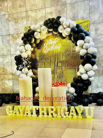 A classic black and white theme for a birthday party. The circular balloon arch is set against a gold shimmer wall, creating a glamorous and high-contrast look.