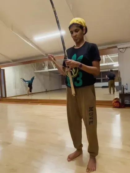 Music is the soul of our classes. Here, a student learns to play the Berimbau, a traditional single-string instrument, while another practices a handstand in the background. This image captures the two core elements of Capoeira: movement and music, working in perfect harmony.