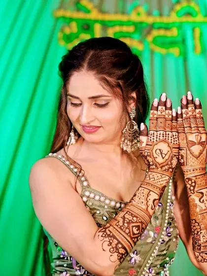 A beautiful client posing with her intricate bridal mehndi. The design includes her and her partner's initials, "AV", inside a heart.