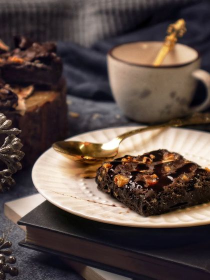 Brownies and coffee make the world a better place. A single brownie is served on a plate, styled with a cup of coffee and old books for a cozy, indulgent, and slightly academic vibe.