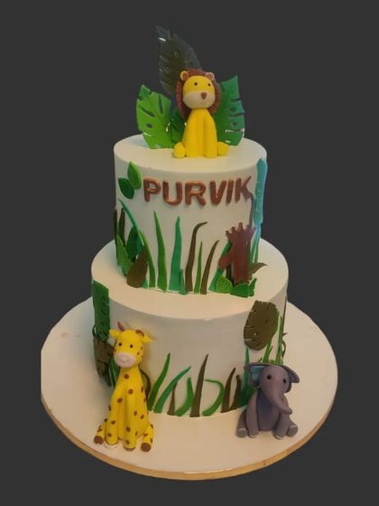 A two-tiered jungle cake with a lion on top and a giraffe and elephant on the bottom tier. The simple design is perfect for a stylish and modern jungle-themed party.