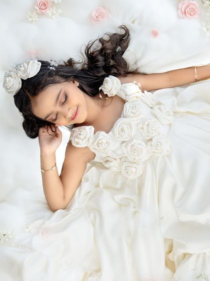 A dreamy, angelic portrait of a seven-year-old birthday girl lying on a bed of clouds, wearing a beautiful white dress adorned with roses.