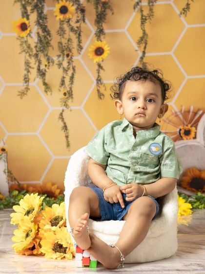 This little boy looks thoughtful before diving into his sunflower-themed cake smash. The yellow and green setup creates a bright and cheerful atmosphere.