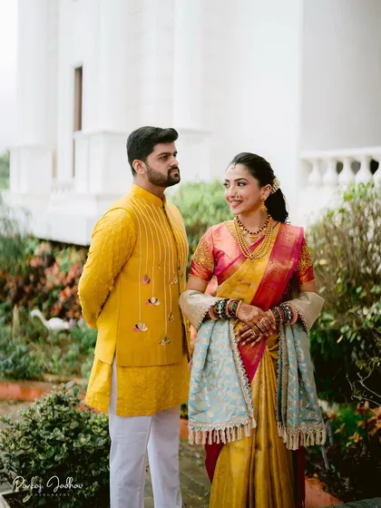 A classic portrait of Maithili and Dhruv at their Satara engagement. Their coordinated yellow and pink outfits stand out beautifully against the elegant white architecture.