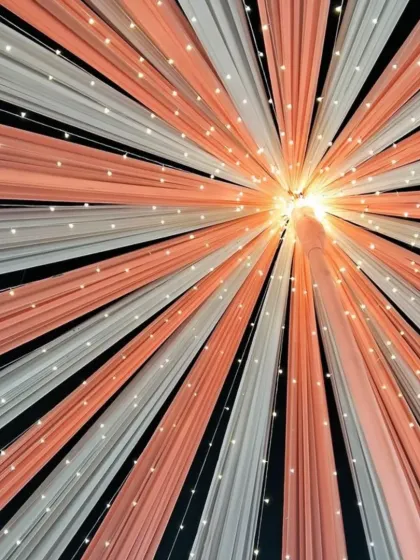 An abstract view of a ceiling decorated with peach and white drapes and fairy lights. This design creates a warm and intimate glow, perfect for an evening reception.