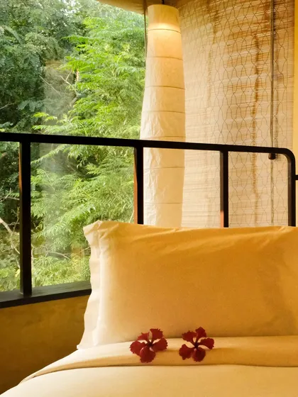 A close-up of a bed in one of our suites, adorned with fresh flowers, overlooking the dense jungle outside.