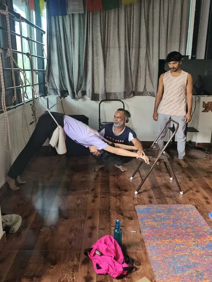 A student uses a chair and wall ropes for a deep stretch in a Downward-Facing Dog variation, a technique from our Iyengar-style practice.