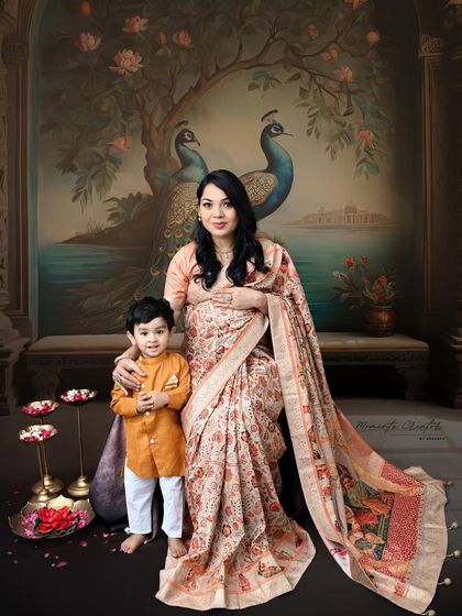 A regal maternity portrait featuring a mother-to-be in a beautiful printed saree with her son. The painted peacock backdrop adds a touch of royal Indian artistry to the session.