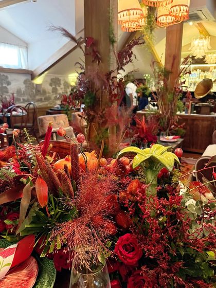 A view across the restaurant space, showing how our floral designs integrate with the venue's decor. The rich red arrangements on the tables and pillars add warmth and luxury to the rustic, wood-paneled room.
