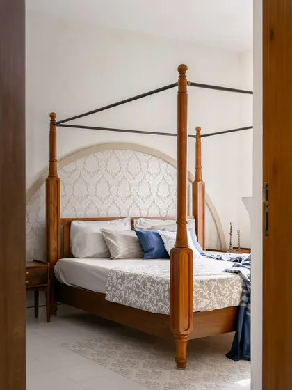 A view into the bedroom, where a classic four-poster bed with an arched, patterned headboard creates an elegant and serene focal point.