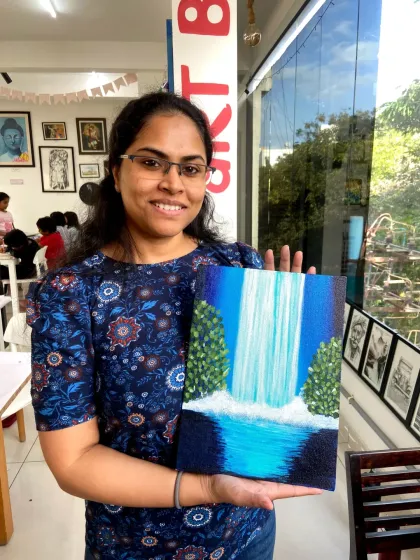 A smiling participant shows off the beautiful waterfall scene she painted on canvas. My guided painting sessions make it easy for anyone to create a masterpiece.
