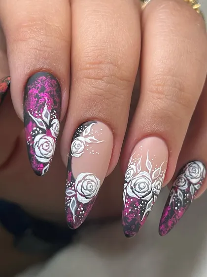 A dramatic Valentine's look with intricate white roses painted over a textured magenta and black background on long almond nails.