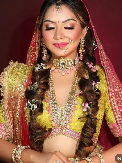 A playful and beautiful hairstyle featuring two textured braids, decorated with small pink flowers. This look is perfect for a Mehendi or Haldi ceremony.