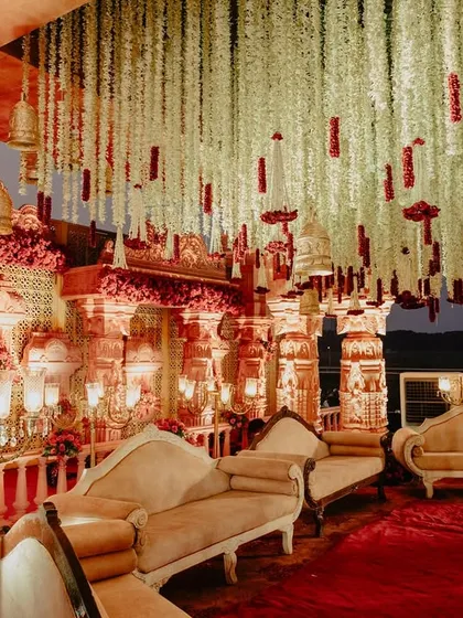 The interior of the temple mandap, featuring plush, traditional seating for the family against a backdrop of carved pillars and hanging florals.