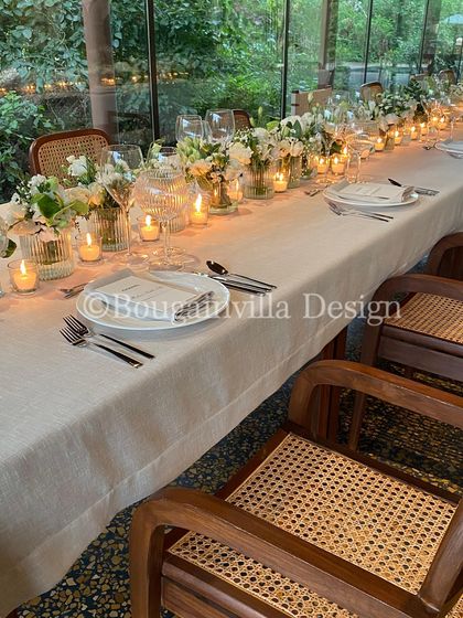 A beautifully set long table for an intimate gathering in our Central Pavilion. The clean white linens, simple glassware, and rows of candles and white flowers create a sophisticated and welcoming atmosphere.