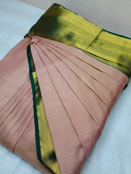 A subtle yet elegant dusty pink silk saree with a green and gold border. The pleats are perfectly ironed and set.