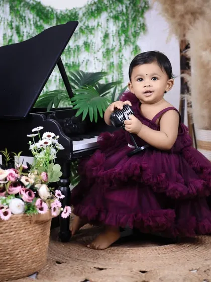 A classic first birthday portrait. This little girl in a stunning ruffled dress holds a toy next to our miniature piano, creating a sophisticated and timeless image.
