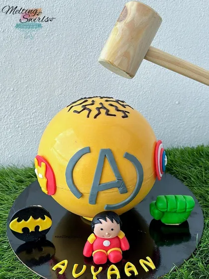 Get ready to smash! This is our super popular superhero pinata cake. The yellow chocolate sphere is decorated with Avengers and Batman logos and comes with a hammer to crack it open, revealing a fun surprise of candies inside.