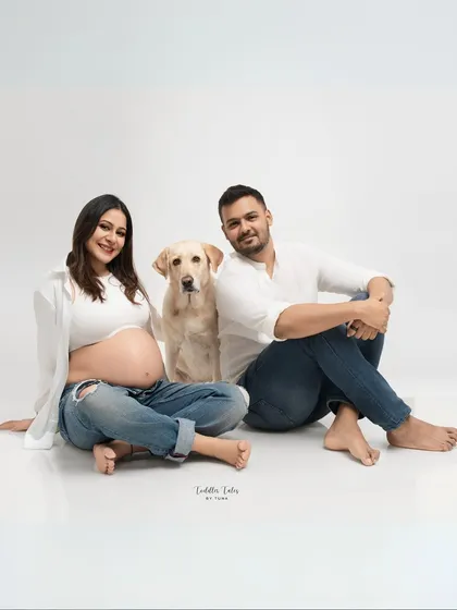 A beautiful family-of-three portrait, with the expecting couple and their dog sitting together, looking confidently at the camera.