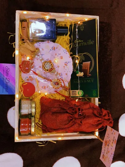 An overhead view of a complete Rakhi hamper. This set includes a rakhi, perfume, dark chocolate, and other traditional elements, making it a perfect package to send your love.
