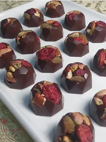 Our fruit and nut bonbons are a celebration of natural ingredients. These geometric dark chocolate shells are filled with a generous mix of toasted nuts and real dried raspberries, offering a perfect balance of rich, tangy, and crunchy.