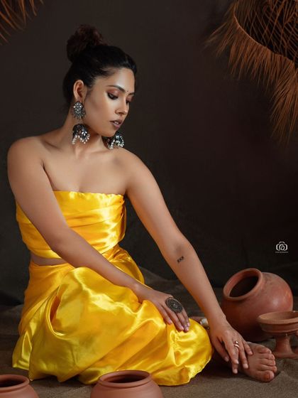 An earthy and rustic studio concept featuring a model in a vibrant yellow satin outfit. The terracotta pots and dark, textured backdrop create a strong visual contrast and a grounded, artistic feel.