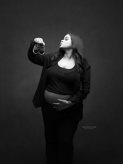 A sweet and playful black and white shot, with the mother-to-be "kissing" a pair of baby shoes. It's a cute way to show her love for the little one.