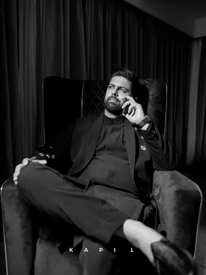 A powerful black and white portrait of the groom, Kapil. The dramatic lighting and relaxed pose in the armchair create a sophisticated and confident image, a perfect memory from his wedding celebrations.