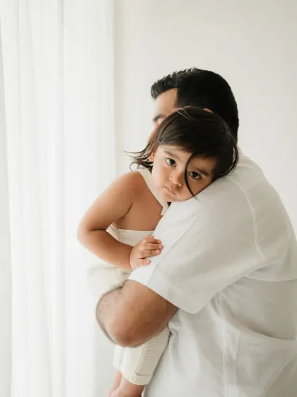 A toddler rests their head on dad's shoulder, looking thoughtfully at the camera. This quiet moment is a beautiful part of any family photoshoot.