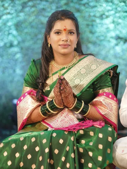 A traditional pose for an engagement ceremony. The client's hands are joined in a 'namaste', and her makeup is soft and respectful of the occasion, paired beautifully with her green Paithani saree.
