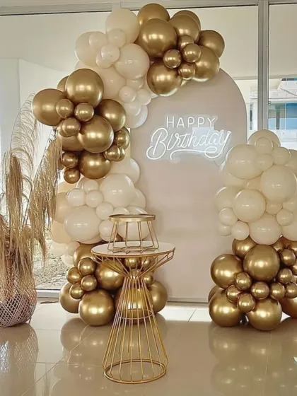 A chic and modern birthday setup with a white arch and neon sign. The arrangement of white and gold chrome balloons is stylish and perfect for a glamorous party.