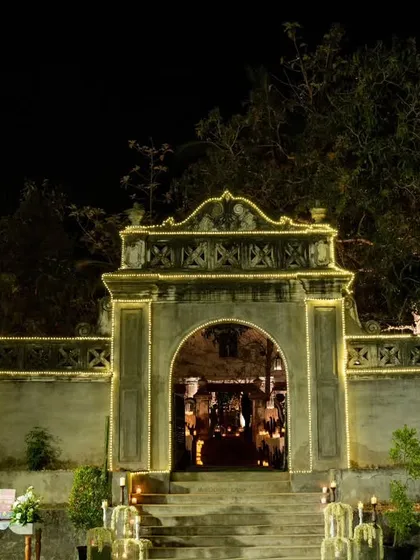 The entrance to a European-inspired wedding in Kerala. The heritage stone gate is outlined with warm lights, welcoming guests up a candlelit staircase to the celebration.