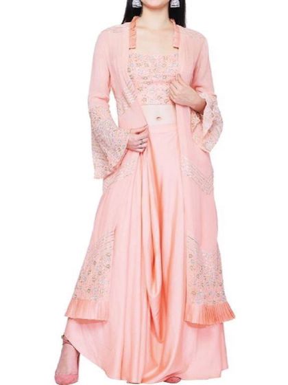 An elegant peach-colored indo-western set featuring dhoti-style pants, an embroidered bustier, and a matching longline jacket with bell sleeves. This is a high-fashion choice for a stylish wedding guest.