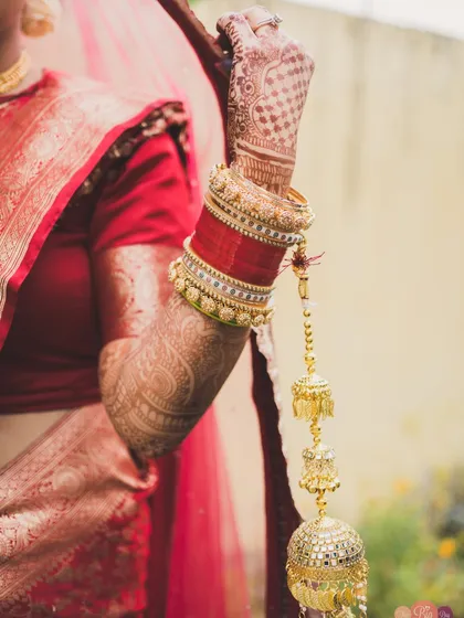 A detail shot of the bride's hands, adorned with intricate henna and traditional red chooda bangles with kalire.