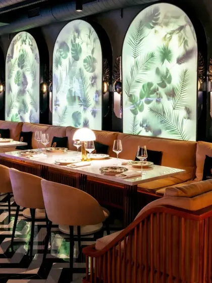 This restaurant design features dramatic, back-lit arched panels with a botanical motif, creating a stunning feature wall. The bold black-and-white chevron floor adds a modern, graphic element to the space.