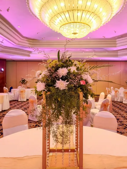 A wider view of the tall centerpiece, showing how it looks on a guest table within the grand ballroom. The cascading greenery and crystals add a touch of elegance and movement.