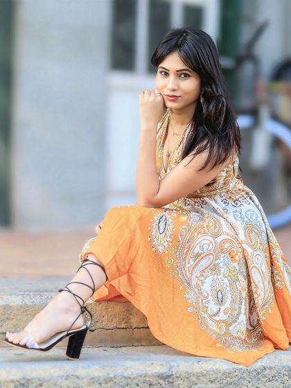 A chic and sophisticated seated pose. The focus is on her elegant posture and the stylish details of her outfit.